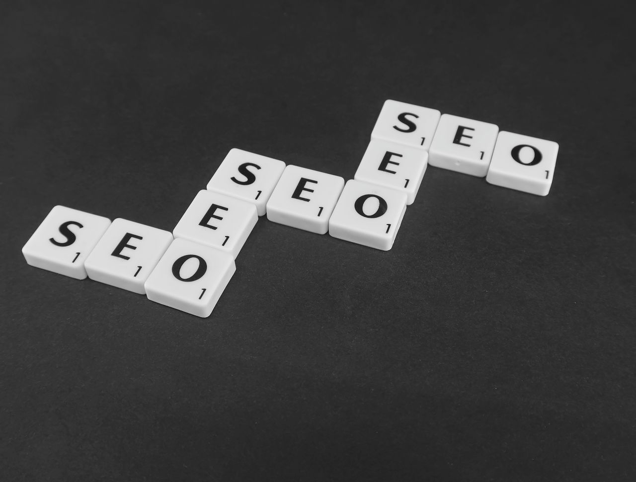 Services-02 SEO spelled with Scrabble tiles on a black surface, representing search engine optimization concepts.